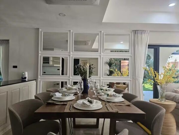 Un coin repas avec une table dressée pour quatre personnes, entourée de chaises, et une vue sur la verdure par la fenêtre.