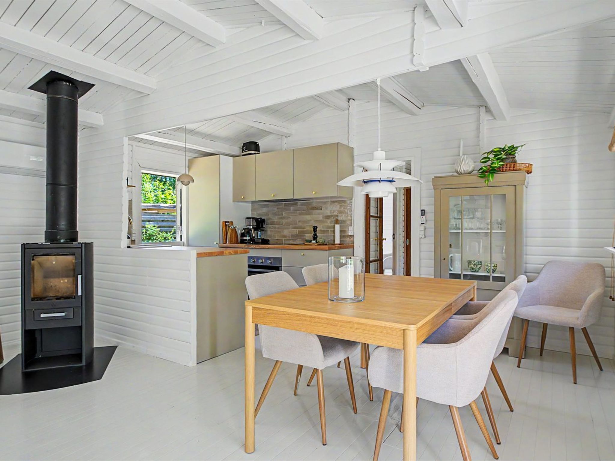 A modern kitchen with a central island, a dining area with a wooden table and chairs, and a built-in wood stove.