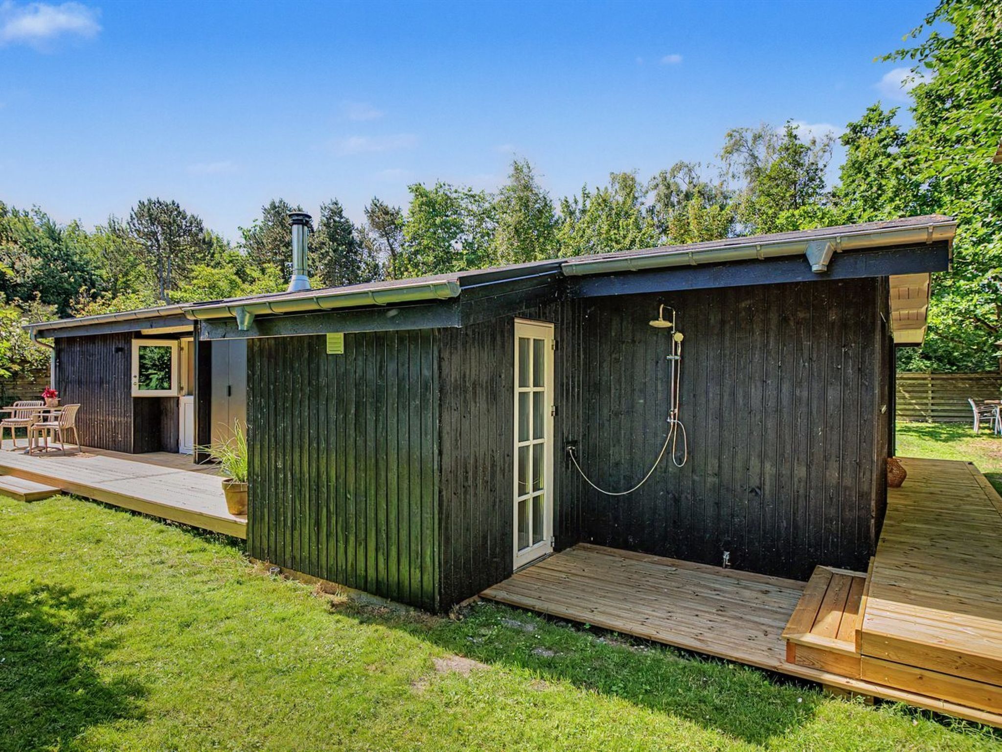 A wooden cabin with a deck, a small patio, and a shower area.