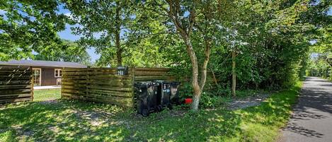 Une structure rustique en bois, ornée du chiffre « 298 » sur une clôture, entourée d’une végétation luxuriante et bordée d’un chemin pavé.