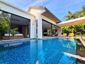 Et moderne hus med swimmingpool, store glasdøre og udendørs møbler.