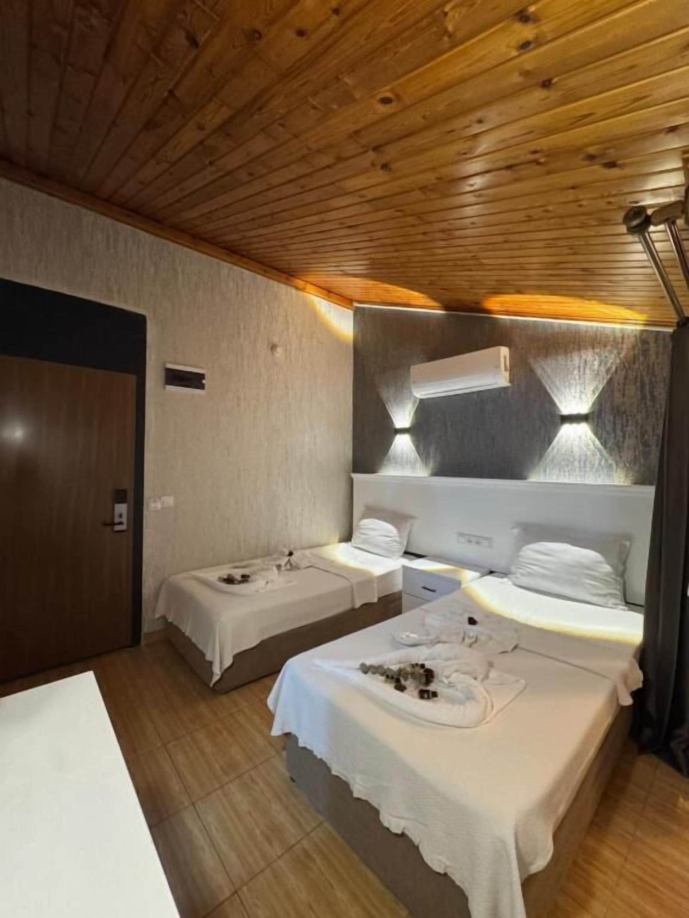 Hotelkamer met houten plafond, twee bedden, een zithoekje en een spiegel met verlichting.