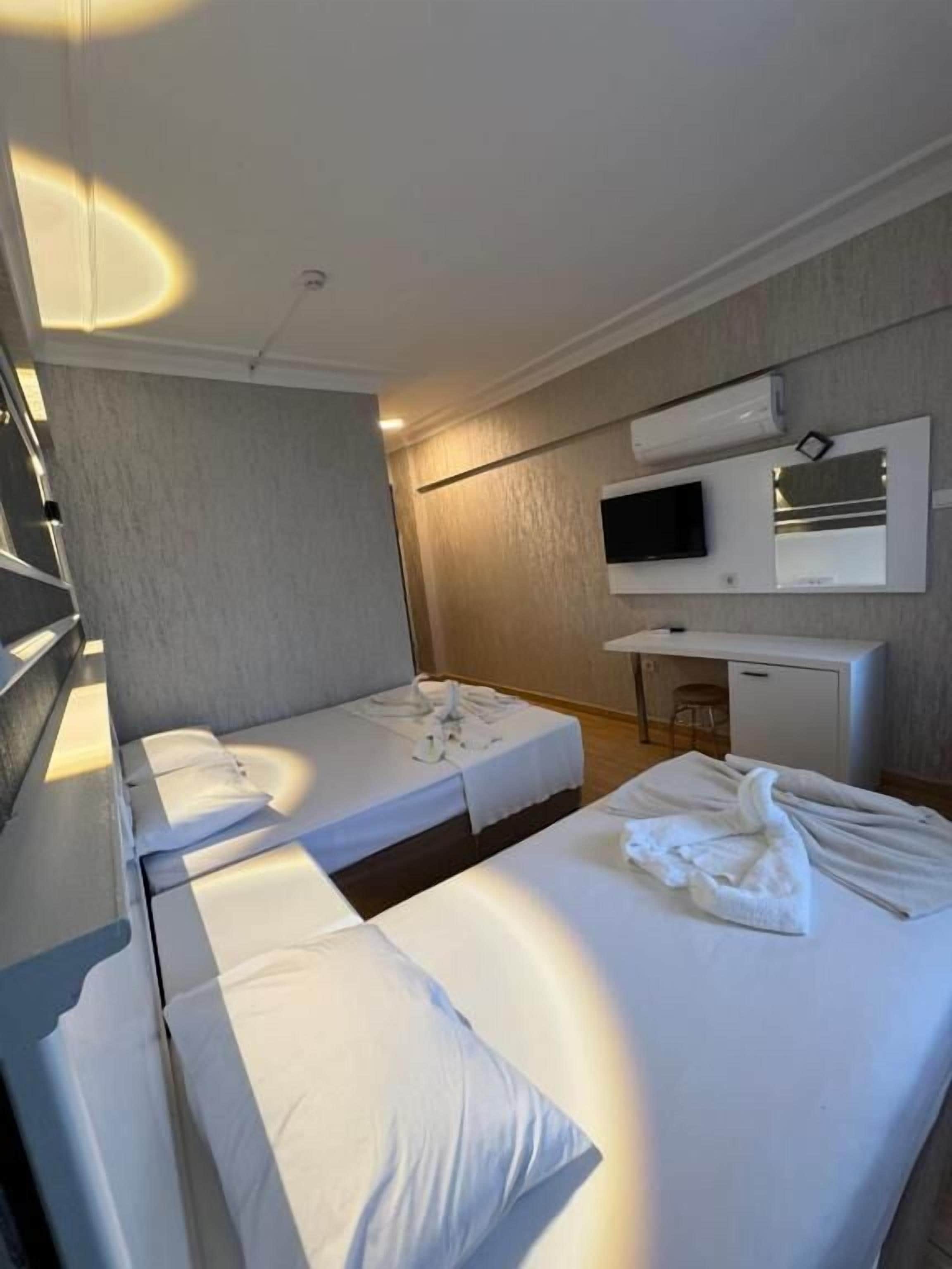 Ein Hotelzimmer mit zwei Betten, einem Flachbildfernseher, einem Schreibtisch und einem Spiegel.