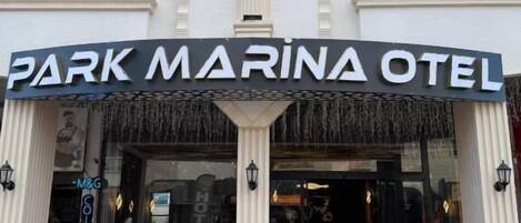 L’extérieur de l’hôtel Park Marina, avec son entrée surmontée d’un tapis rouge, une enseigne et un balcon.