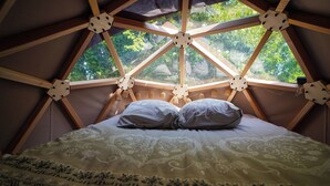 A room with a geometric wooden ceiling, a bed with patterned bedding, and a view of greenery outside.