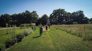 A grassy outdoor area with a pathway, trees, and a small structure.