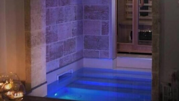 Ein Zimmer mit Stehwänden, einem blau beleuchteten Pool und einer Treppe, die zu einer Tür führt.