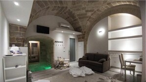Ein Zimmer mit Steindecke, einer Couch, einem Tisch und einem Fernseher.