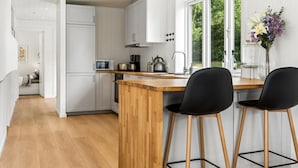 Una cucina moderna con mobili bianchi, un'isola in legno, sgabelli da bar neri e una finestra vista verde.