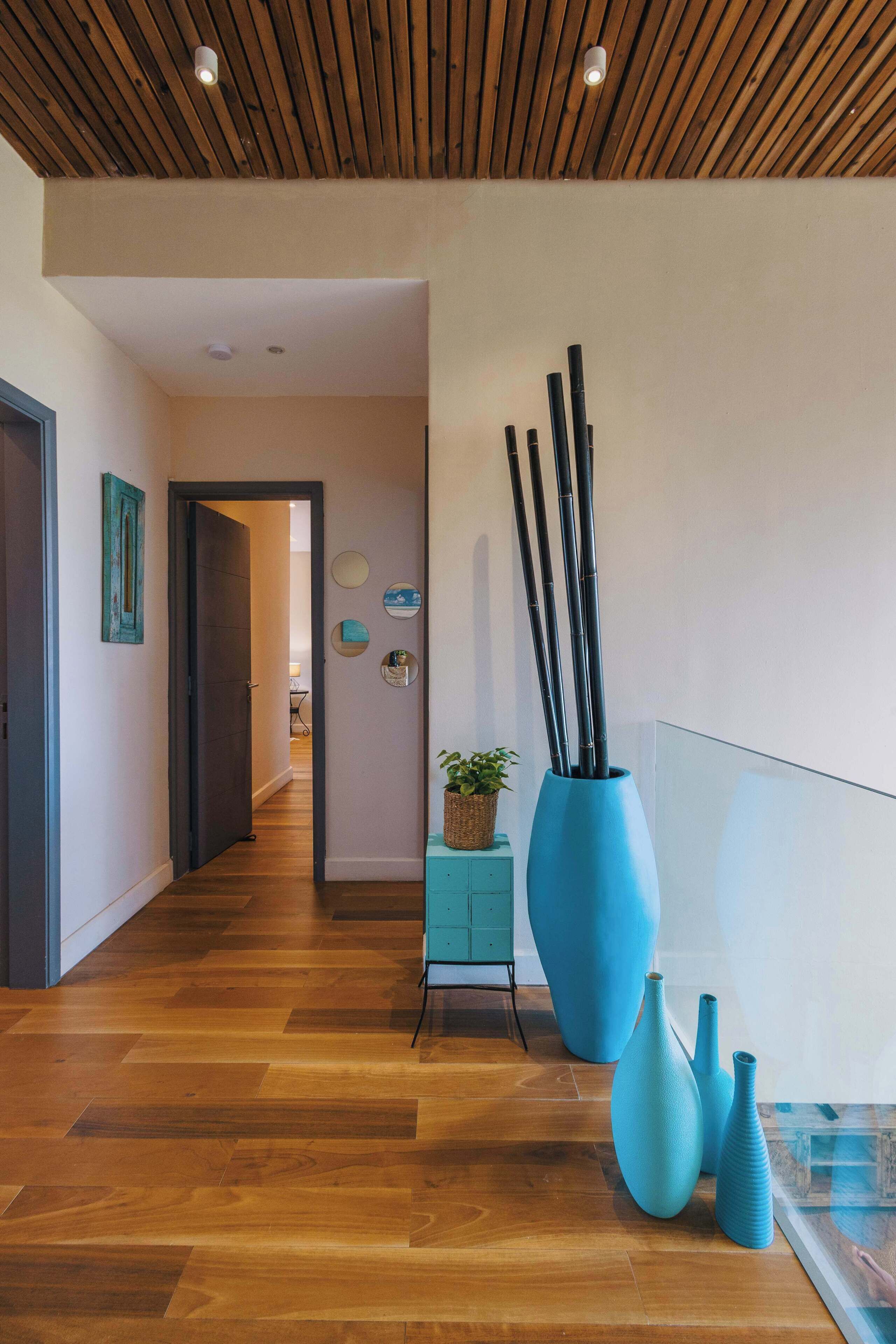 A hallway with wooden flooring, a blue vase, and a small cabinet.