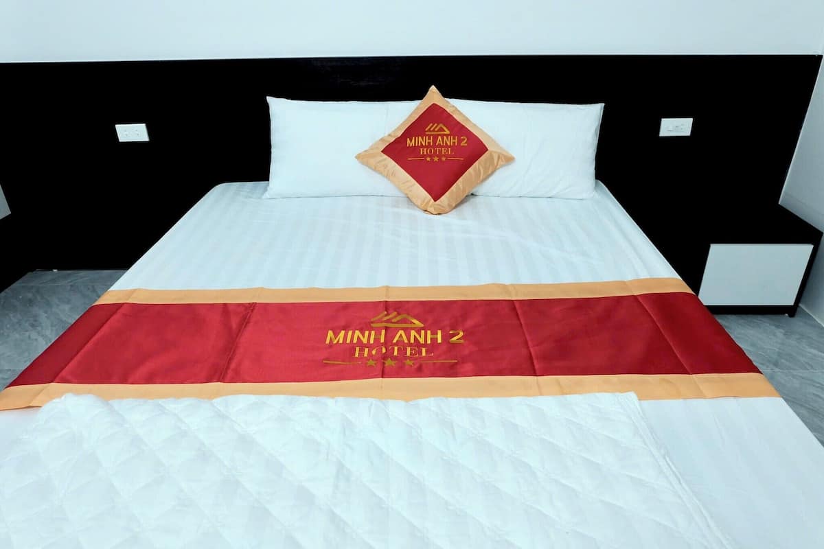 A bed with a white bedspread, a red and gold hotel logo, and a black headboard.