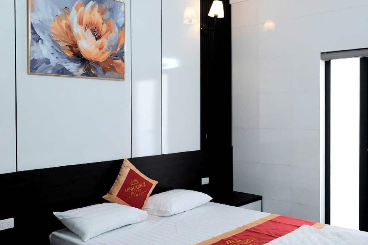 A modern hotel room with a bed, a wall-mounted painting, a bedside lamp, and a view of the outside.