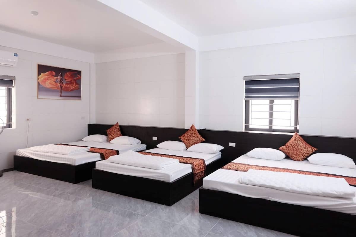 A hotel room with four beds arranged in a row, white walls, and a large window with blinds.