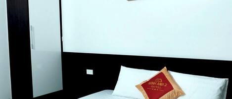 A hotel room with a bed, a red and gold bedspread, a pillow with hotel branding, a wardrobe, and a wall art piece.
