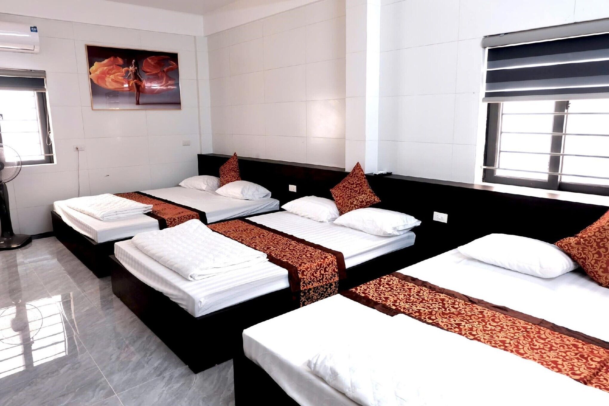 Habitación de hotel con tres camas, un ventanal grande, aire acondicionado de pared y un cuadro.