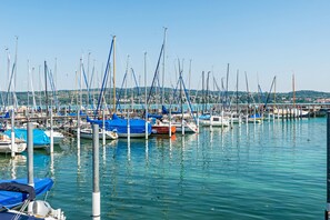 A marina with multiple boats docked, calm water, and a distant view of a town.