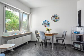 A modern kitchen with a dining table, chairs, a radiator, a wall-mounted heater, and a shelf with a toaster.
