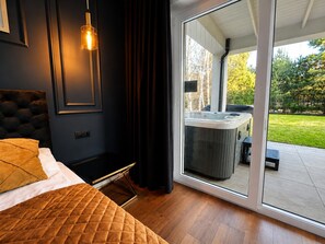 A bedroom with a bed, a hanging light, a sliding glass door leading to an outdoor hot tub area. - Large Holiday Home, Swimming Pool, Sauna, Jacuzzi (Krokowa)