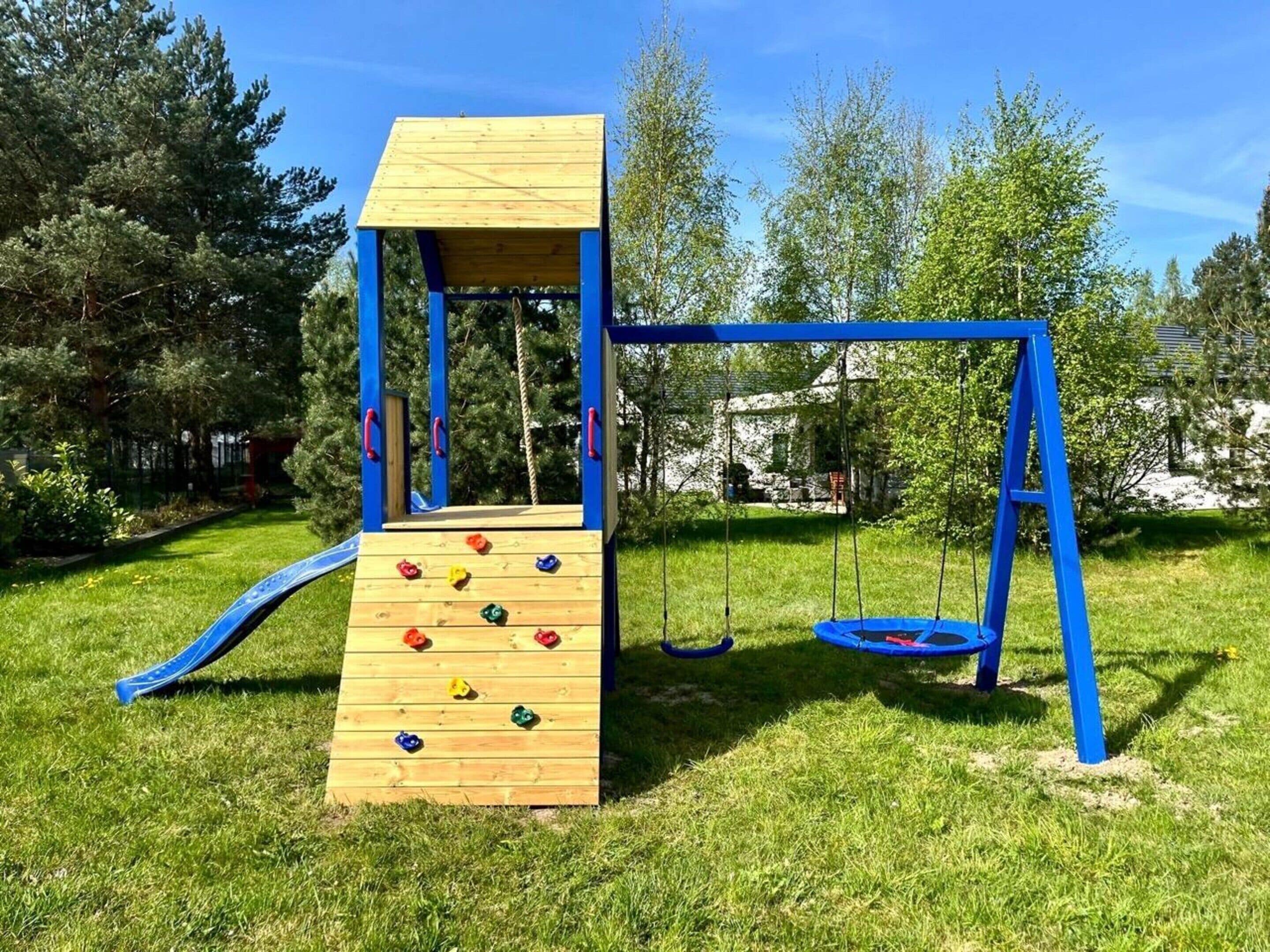 A playground with a wooden climbing wall, swings, and a slide.