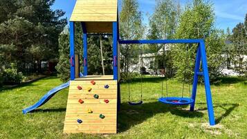 A playground with a wooden climbing wall, swings, and a slide.