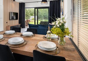 A dining area with a wooden table set for four, a television mounted on the wall, and a sofa in the background. - Large Holiday Home, Swimming Pool, Sauna, Jacuzzi (Krokowa)