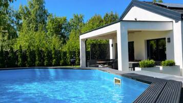 A modern outdoor pool area with a covered seating area and a wooden deck.