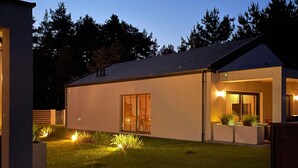 Ett modernt hus med en välskött gräsmatta, ett stort fönster och en liten veranda.