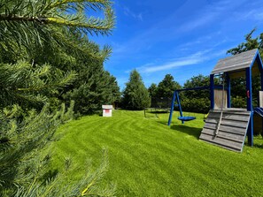 A playground with a swing set and a slide, surrounded by green grass and trees. - Large Holiday Home, Swimming Pool, Sauna, Jacuzzi (Krokowa)