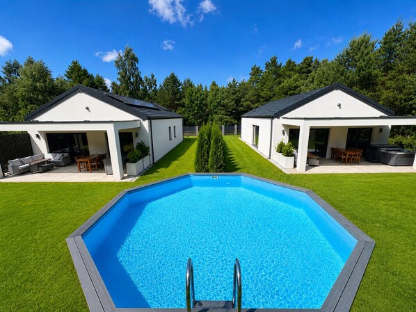 A swimming pool with a wooden deck, two adjacent buildings with outdoor seating, and a well-maintained lawn. - Large Holiday Home, Swimming Pool, Sauna, Jacuzzi (Krokowa)