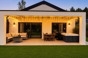 Un patio exterior moderno con jacuzzi, zona de estar y luces colgantes.