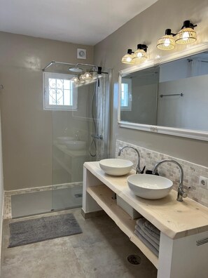 Un bagno moderno con cabina doccia in vetro, due lavabi, un grande specchio e illuminazione a sospensione.