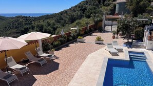 A pool area with lounge chairs and umbrellas, surrounded by a tiled patio and a view of the sea. - Villa Melin - Panoramic Views, Privacy, and a Heated Pool (Torrox)