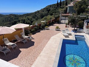 A pool area with lounge chairs and umbrellas, surrounded by a tiled patio and a view of the sea. - Villa Melin - Panoramic Views, Privacy, and a Heated Pool (Torrox)