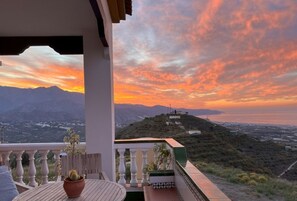 Un balcone con vista su un tramonto montano, un tavolo con una pianta e una ringhiera.