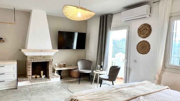 A bedroom with a fireplace, two chairs, a bed, a TV, and a view of the outdoors. - Villa Melin - Panoramic Views, Privacy, and a Heated Pool (Torrox)
