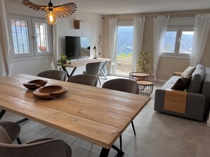 A modern living room with a wooden dining table, grey sofa, and a TV. - Villa Melin - Panoramic Views, Privacy, and a Heated Pool (Torrox)