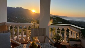 A balcony with a view of the sunset over a coastal landscape, including mountains and a body of water. - Villa Melin - Panoramic Views, Privacy, and a Heated Pool (Torrox)