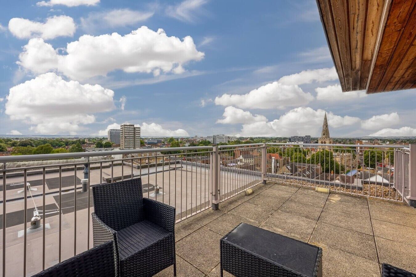 Een terras op het dak met buitenmeubilair, uitzicht op de stad en een kerktoren in de verte.