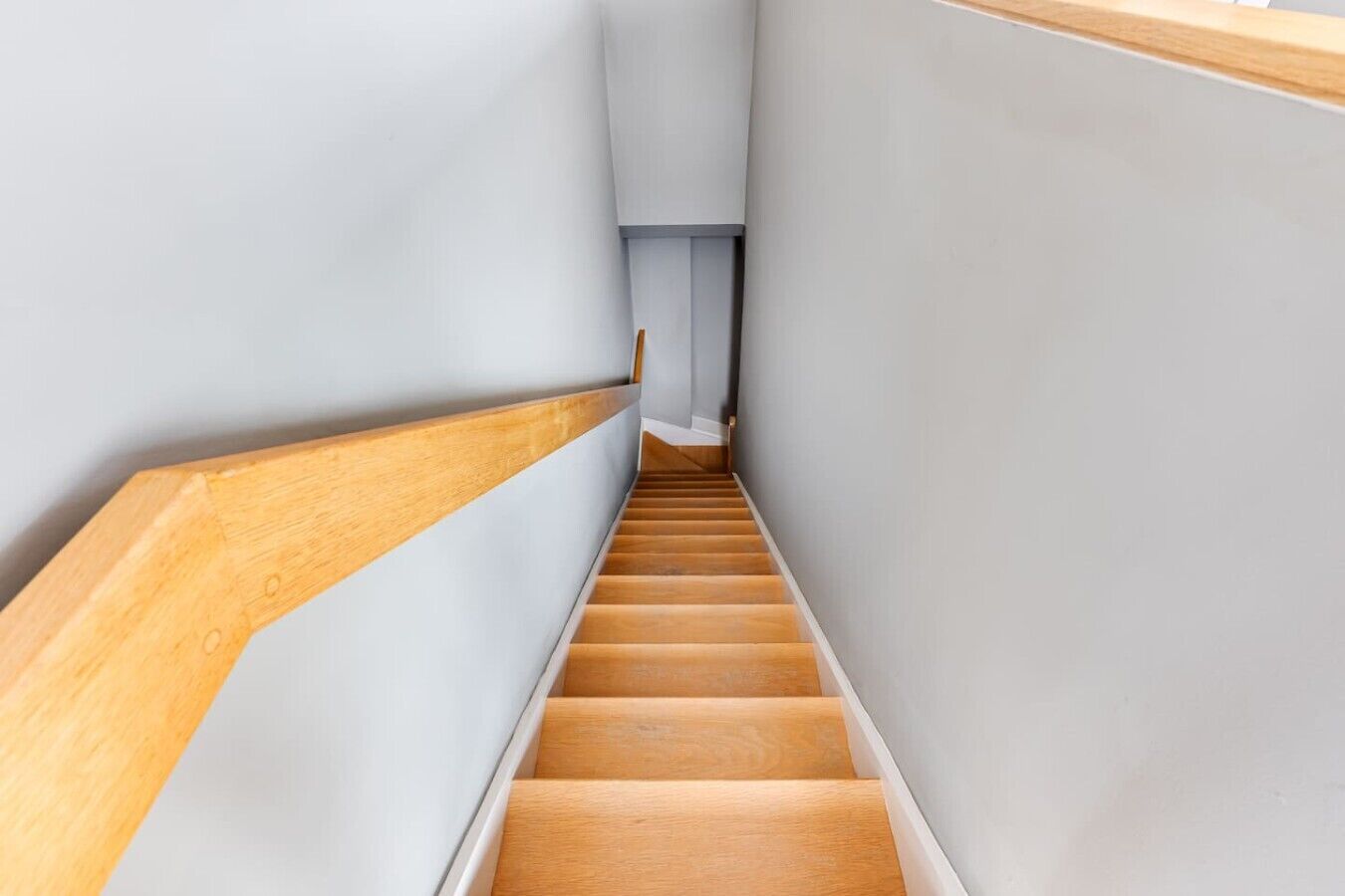 A narrow staircase with wooden steps and white walls.