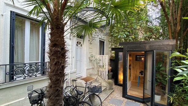 A courtyard with a palm tree, bicycles, a small wooden structure, and a white building with black-framed windows. - Family home just a stone's throw from Paris, with a garden and a hammam (Asnières-sur-Seine)