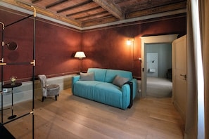 Una habitación con un sofá azul, una mesita con una lámpara y una silla.
