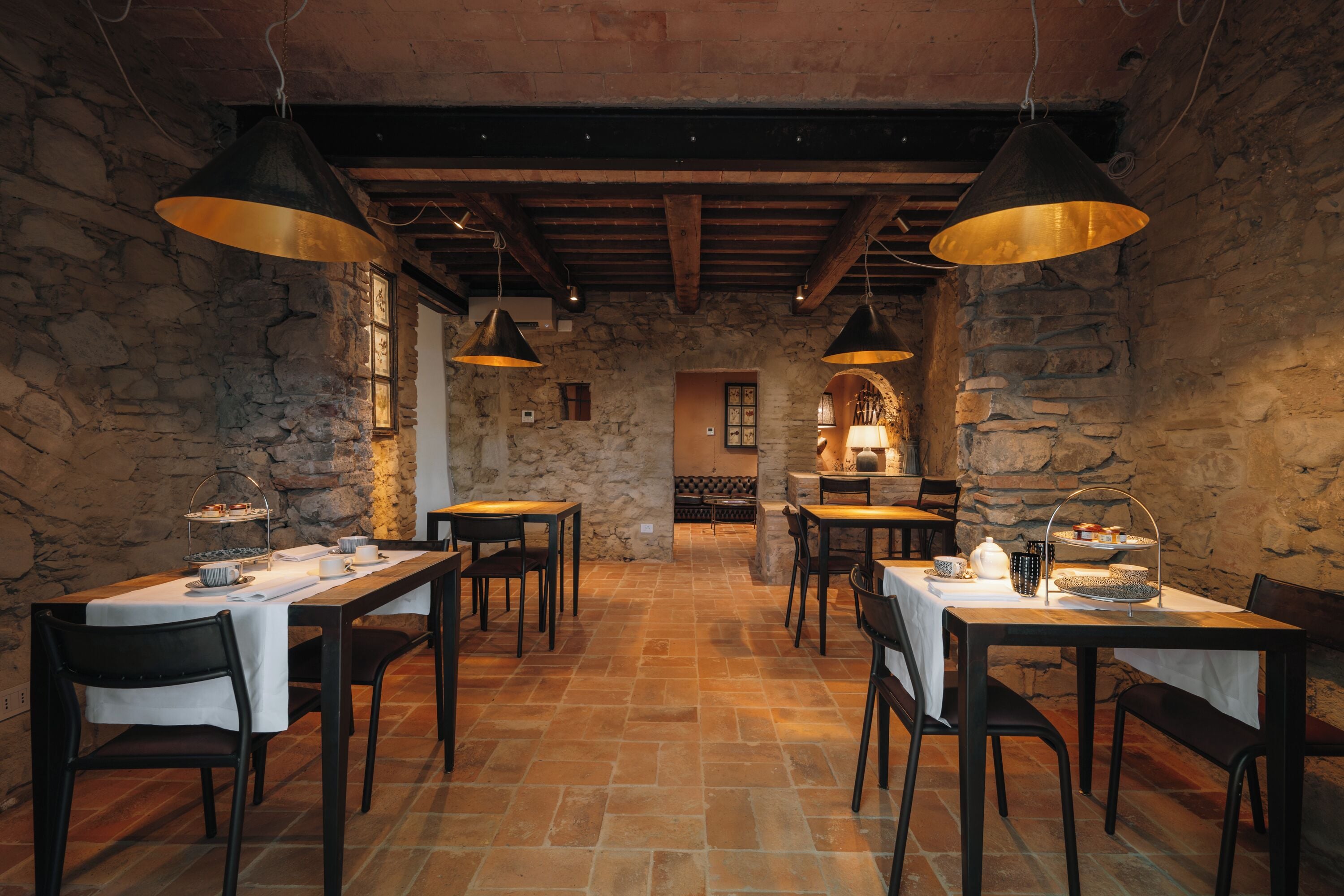 A rustic dining area with stone walls, wooden tables, and hanging pendant lights.