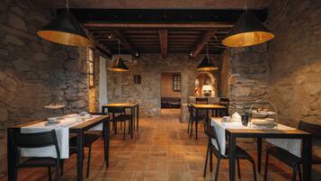 A rustic dining area with stone walls, wooden tables, and hanging pendant lights.