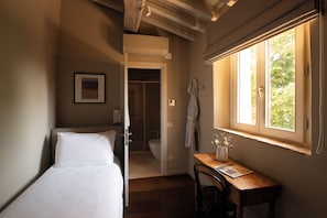 A bedroom with a single bed, a wooden desk, a window with a view, and a door leading to a bathroom.