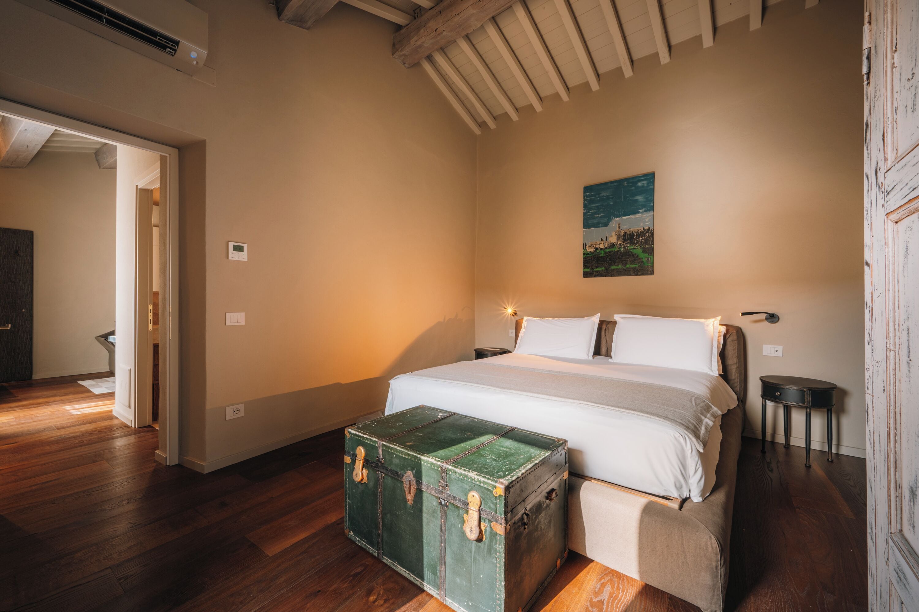 Un dormitorio con una cama grande, un baúl verde y un cuadro en la pared.