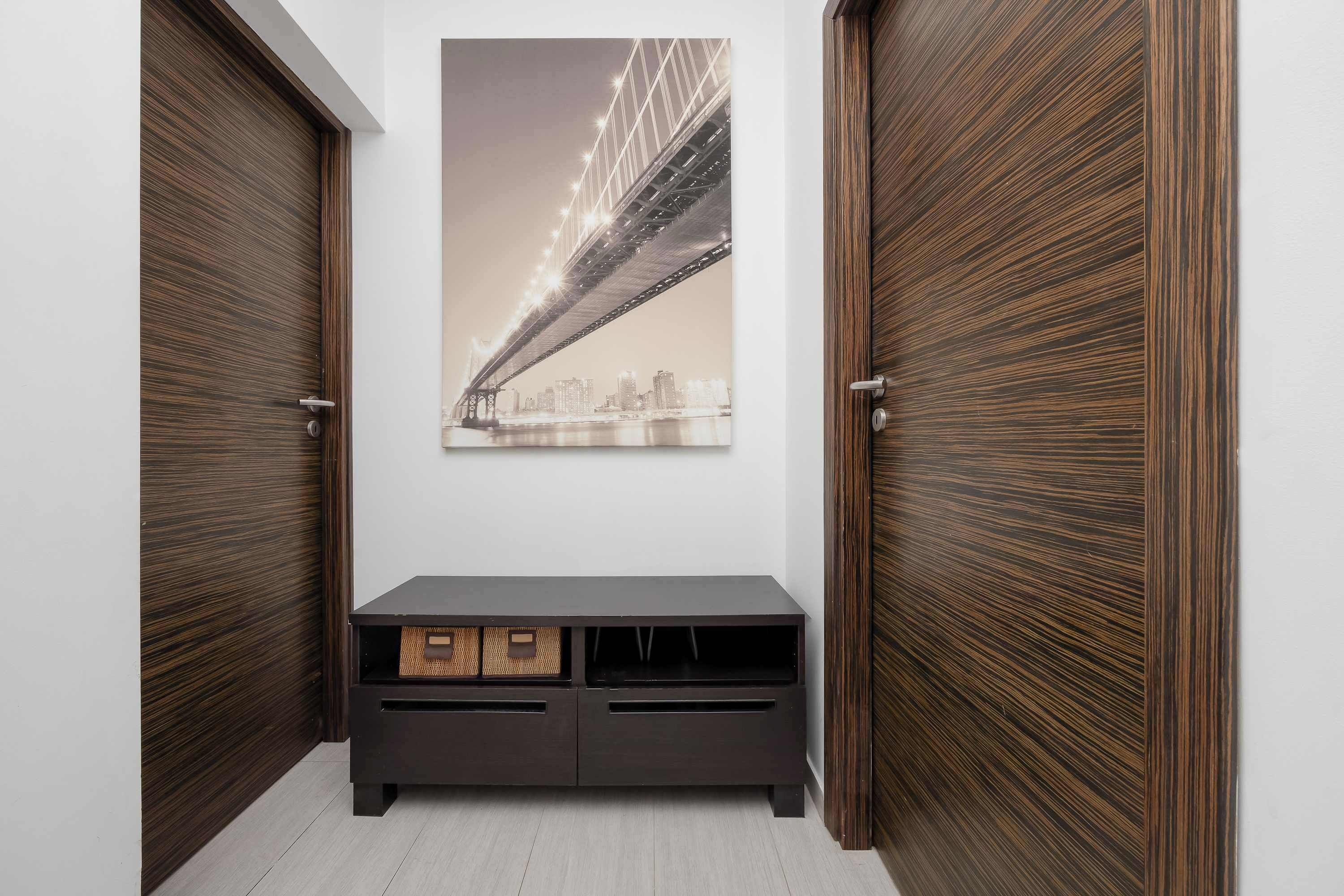 A hallway with wooden doors, a small bench, and a decorative wall picture. The bright interior has a clean and modern design.