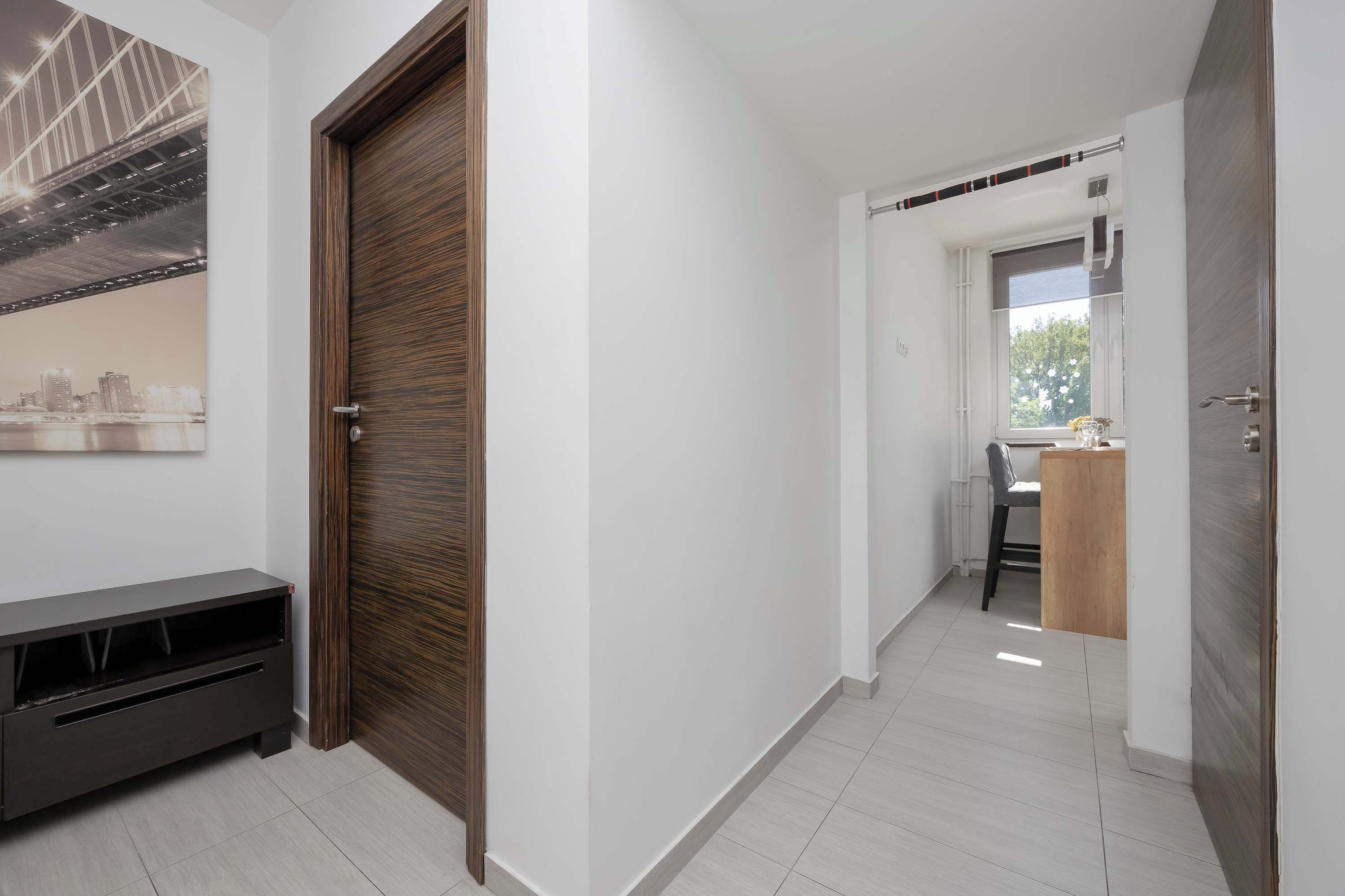 A hallway with a wooden door, a TV stand, and a window with a view of the outside.