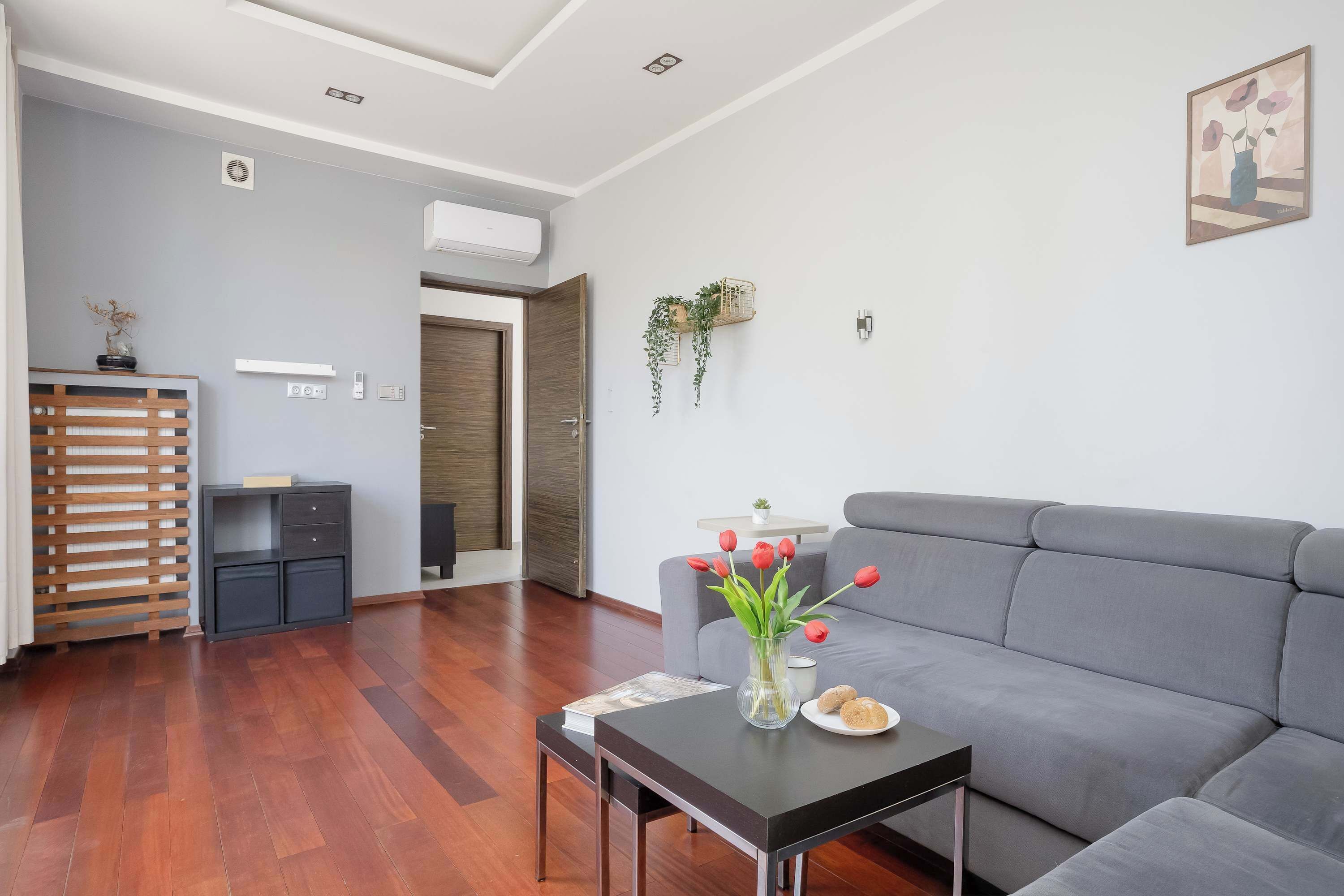 Una sala de estar moderna con un sofá gris, una mesa de centro de madera y un jarrón con flores rojas.