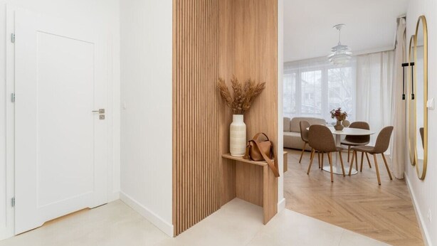 Een modern interieur met een houten scheidingswand, een eethoek met stoelen en een tafel, en een witte deur.