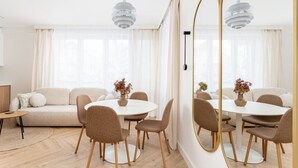 Een moderne woonkamer met een bank, een ronde eettafel, stoelen en een grote spiegel.